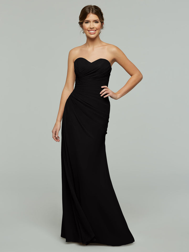 A woman smiles in the Avery Austin TH-80028, a black strapless chiffon gown with sweetheart neckline and ruched bodice, posing with one hand on her hip against a plain light gray background.