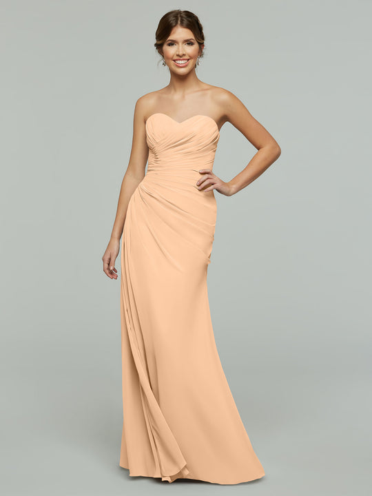 A woman models the Avery Austin 80028 dress in blush—a strapless, floor-length chiffon gown with a ruched bodice, draped skirt, and subtle sweetheart neckline—posing against a plain gray background.