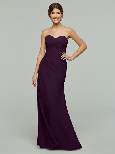Model wearing Avery Austin’s strapless, floor-length chiffon dress (Style 80028) in dark purple, featuring a ruched bodice and subtle sweetheart neckline, smiling against a plain gray background.