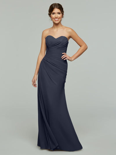 A woman poses against a light gray background wearing Avery Austin’s 80028, a strapless, floor-length chiffon dress with a sweetheart neckline and ruching detail.