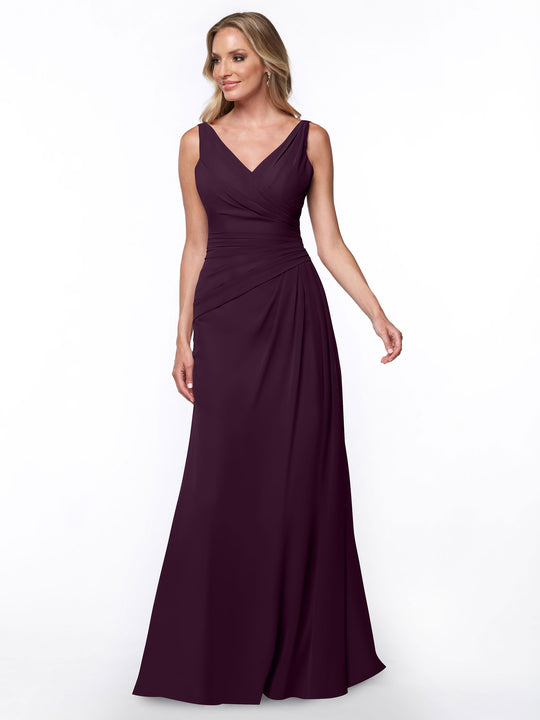 A woman in Avery Austin’s aubergine 80030 sleeveless, floor-length sheath dress with a V-neck and ruched bodice stands against a plain white background.
