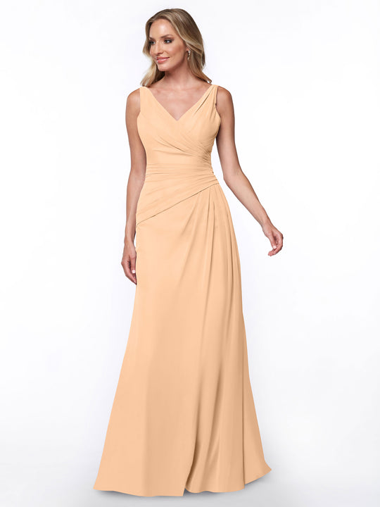 A woman wearing Avery Austin’s 80030 sheath dress in blush, featuring a sleeveless design, floor-length hem, V-neckline, and ruched bodice, stands against a plain white background.