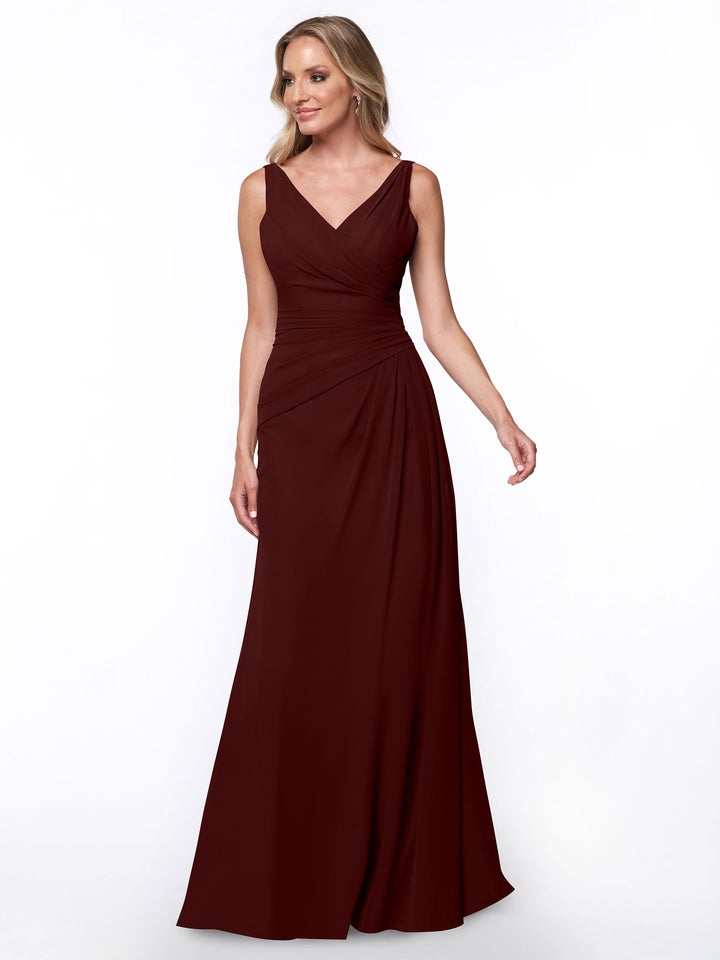 A woman wears Avery Austin style 80030, a merlot sleeveless sheath gown with ruched bodice and V-neckline, standing against a plain white background.