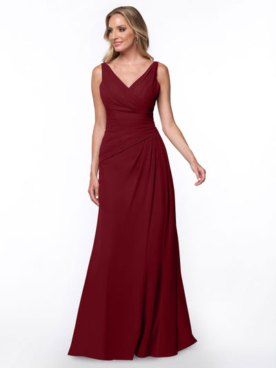 A woman wears Avery Austin’s 80030, a sleeveless floor-length burgundy sheath dress with a V-neckline and ruched bodice, standing against a plain white background.