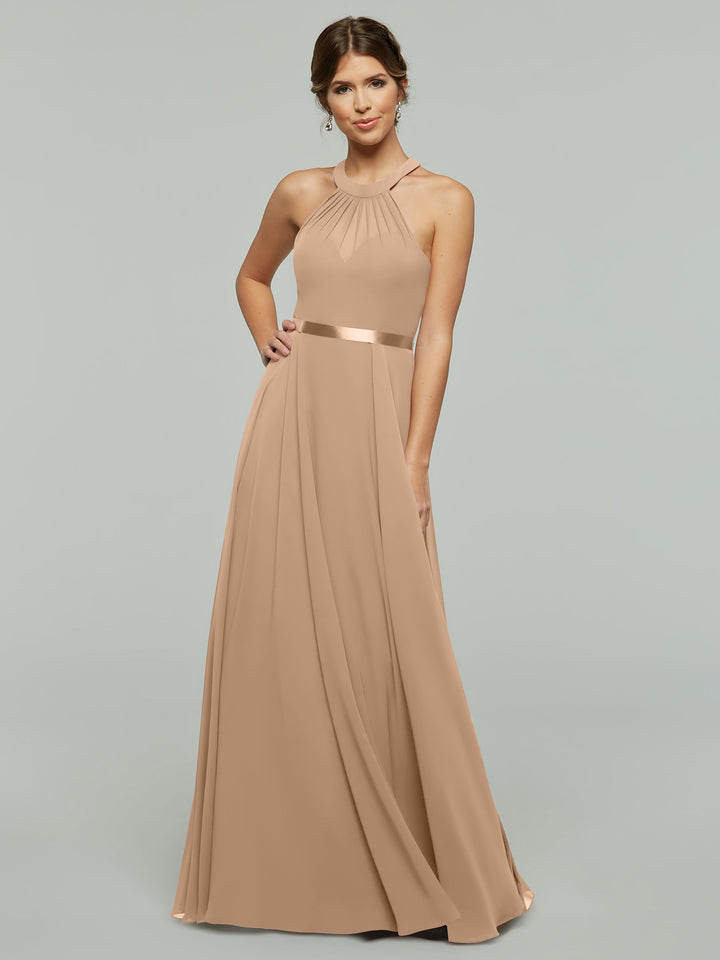 A woman models Avery Austin style 80038, an A-line chiffon dress in buff with a sleeveless halter neckline, satin waistband, and floor-length pleated skirt, standing against a light gray background.