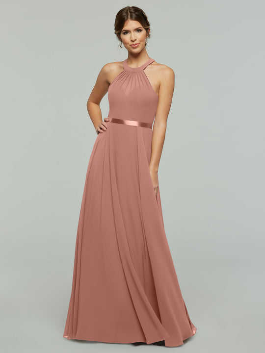A woman wearing Avery Austin’s 80038, a sleeveless dusty rose chiffon A-line gown with halter neckline and satin waistband, stands smiling against a light gray background with one hand on her hip.