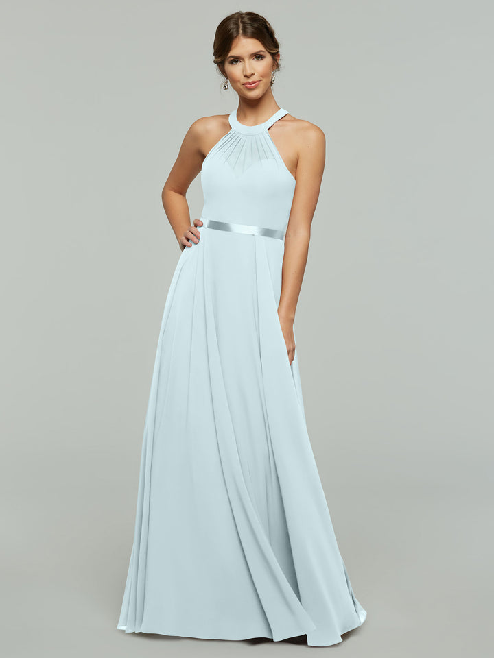 A woman poses against a plain gray background wearing Avery Austin’s 80038: a light blue, floor-length A-line chiffon dress with a halter neckline, pleated detailing, and a satin waistband.