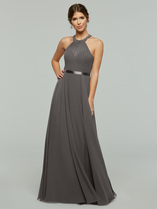 A woman modeling Avery Austin style 80038, a sleeveless floor-length dark gray chiffon A-line dress with halter neckline and satin waistband, stands against a light gray background.