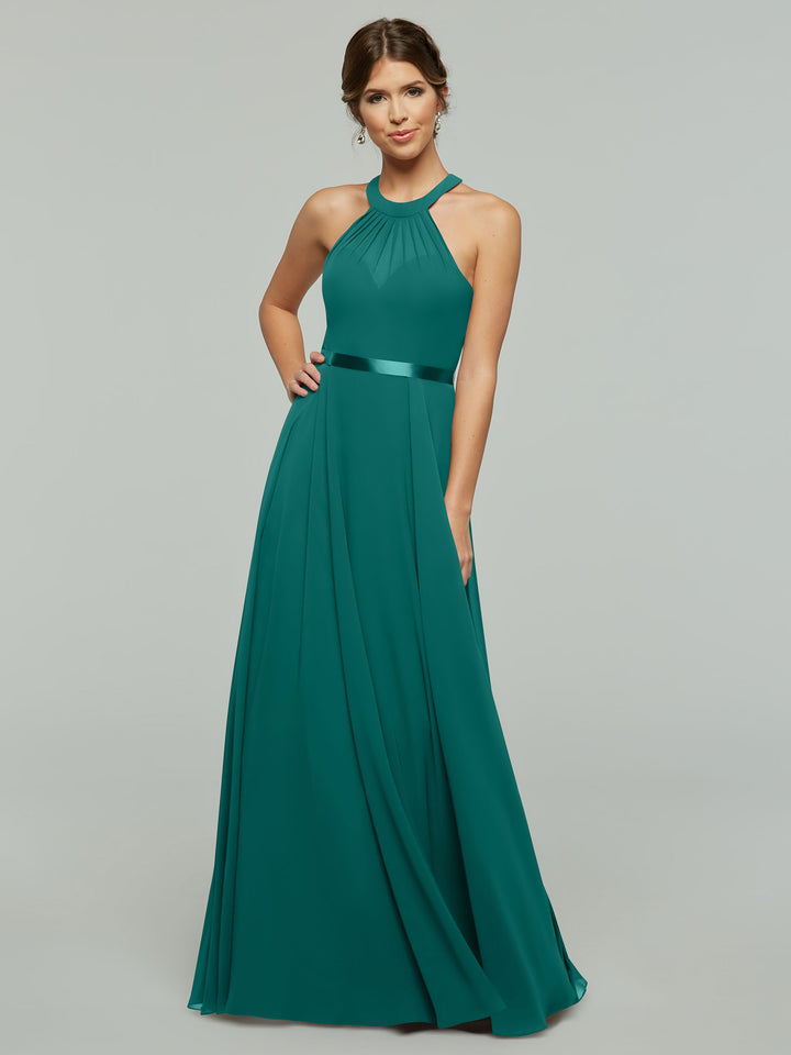 A woman wears a flowing teal halter-neck evening gown with a satin waistband and elegant draping.