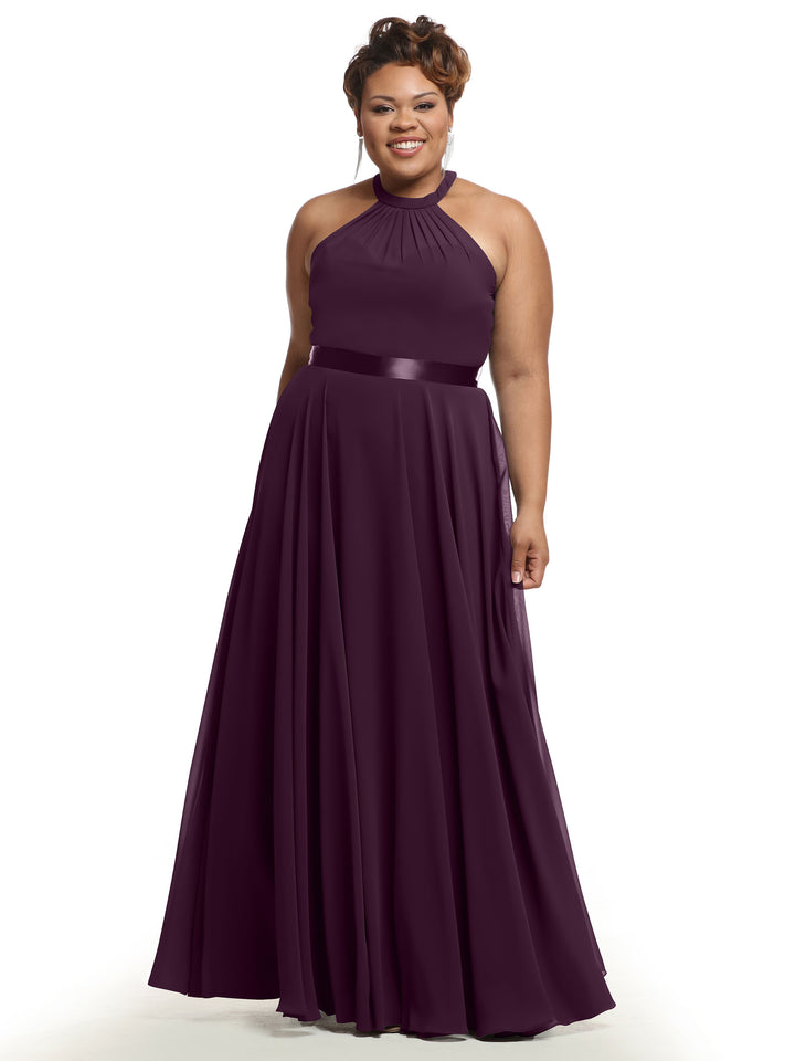 A woman smiles against a plain white background in Avery Austin’s 80038, a sleeveless, floor-length A-line chiffon dress in aubergine with a halter neckline and pleated skirt.