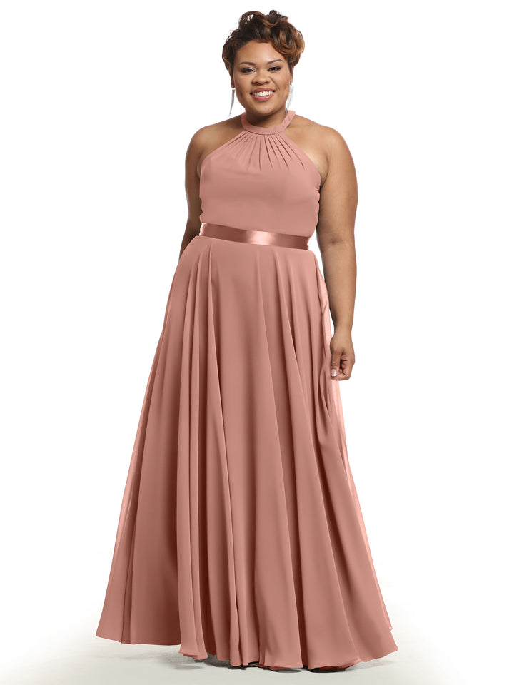 A woman stands smiling against a white background, wearing Avery Austin’s 80038—a sleeveless, floor-length dusty rose A-line chiffon dress with a halter neckline, gathered bodice, pleated skirt, and satin waistband.