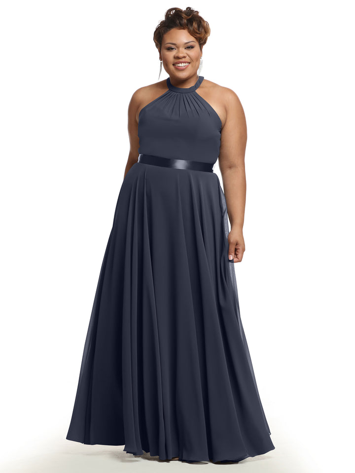 A woman smiles against a white background wearing Avery Austin’s 80038—a floor-length, sleeveless navy A-line chiffon dress featuring a halter neckline and fitted waistband.