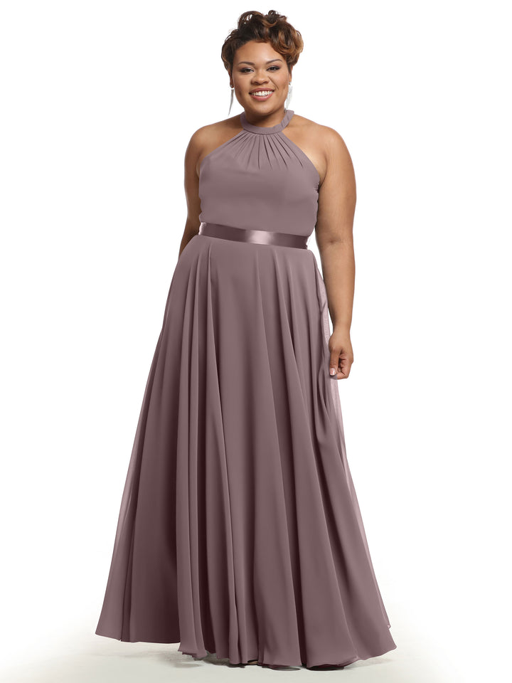 A smiling woman wears Avery Austin’s 80038 A-line chiffon dress with a halter neckline, pleated bodice and skirt, and satin waistband, standing against a white background.