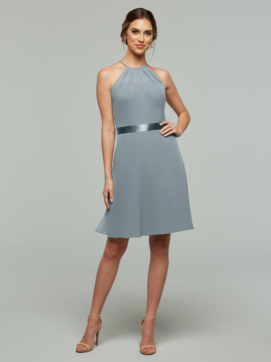 A woman models Avery Austin style 80042—a light blue, sleeveless, knee-length dress with an A-line chiffon skirt and satin waistband—posing confidently in nude heels against a plain gray background.
