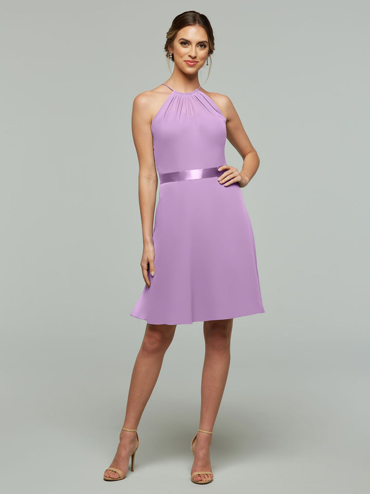 A woman models Avery Austin’s 80042: a sleeveless, knee-length lavender dress with a halter neckline, A-line chiffon skirt, satin waistband, and nude high heels against a plain background.