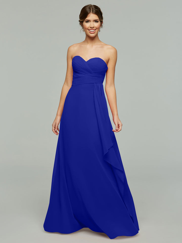 A woman smiles in Avery Austin’s 80046, a royal blue strapless chiffon dress with a sweetheart neckline, fitted ruched bodice, elegant draping, and floor-length skirt, set against a plain light gray background.