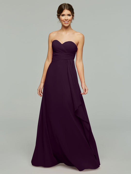 A woman smiles in the Avery Austin 80046, a timeless floor-length strapless chiffon dress with elegant draping and a sweetheart neckline, set against a plain light gray background.