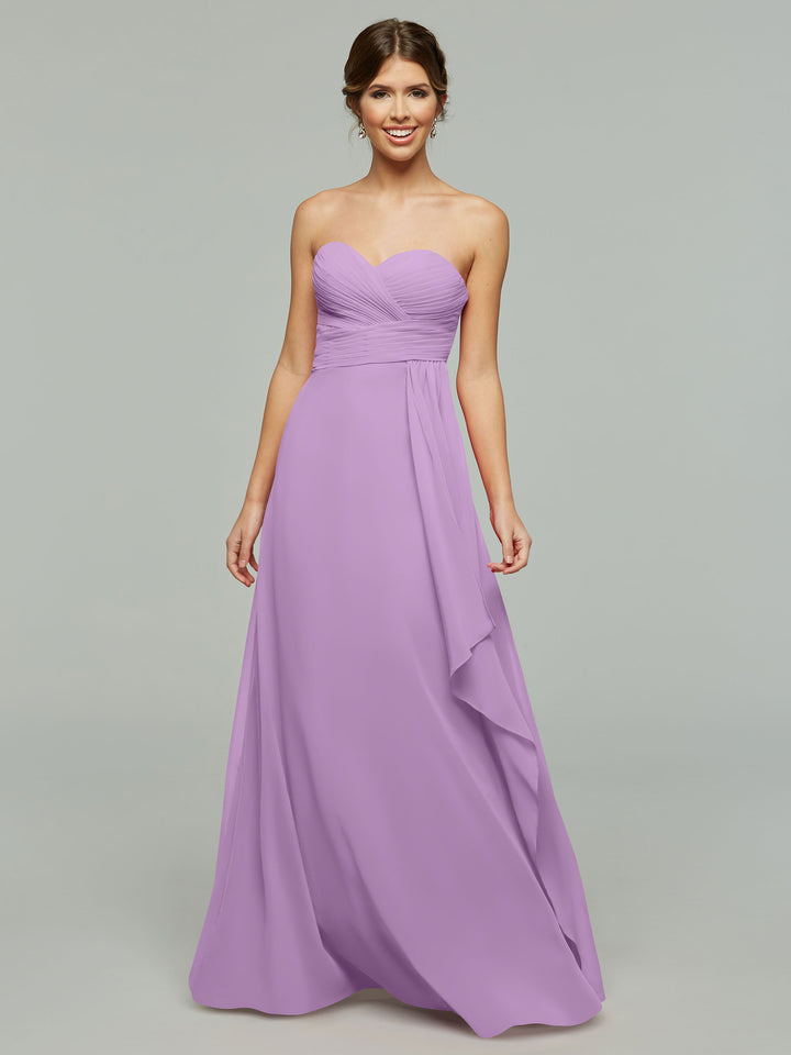 A woman models Avery Austin 80046—a strapless lavender chiffon dress with a sweetheart neckline, elegant draping, and ruched bodice—standing against a plain light gray background for a timeless look.