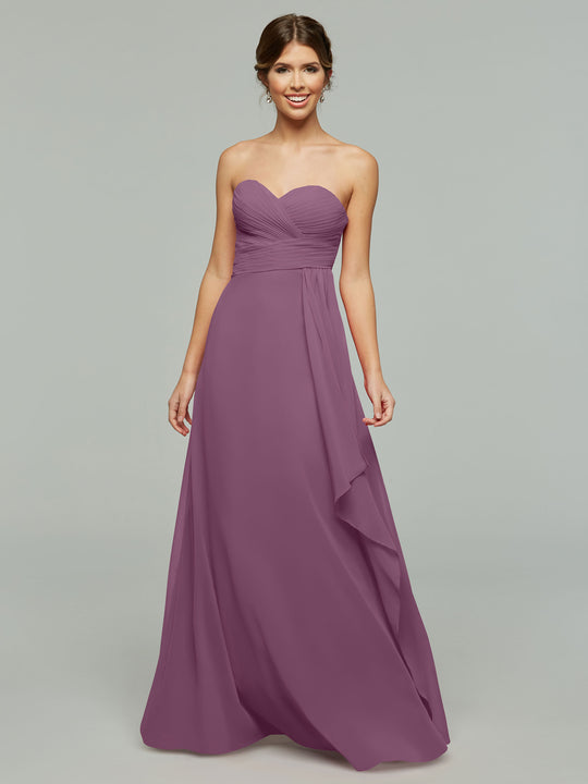 A woman smiles in a mauve Avery Austin 80046 strapless chiffon dress featuring a sweetheart neckline, ruched bodice, and elegant draping. She stands against a plain light gray background.