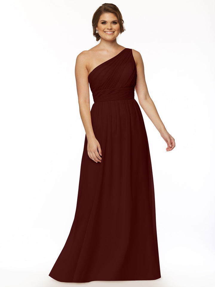 A woman stands against a white background, smiling softly in the Avery Austin TH-80047 merlot floor-length one-shoulder chiffon dress featuring a gently ruched bodice, her right arm relaxed at her side.
