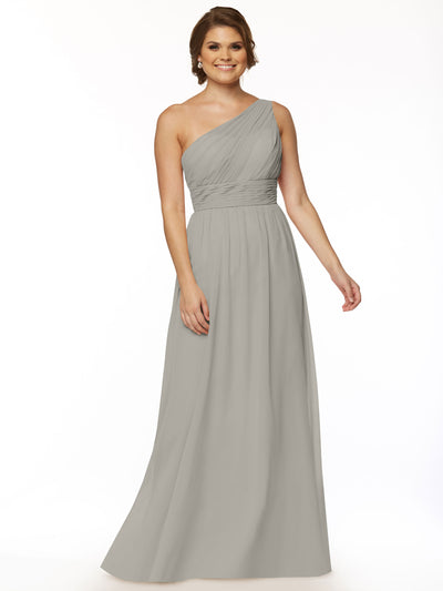 A woman stands smiling against a plain white background, wearing Avery Austin’s 80047: a long, light gray chiffon one-shoulder dress with a fitted, ruched bodice and a flowing skirt.