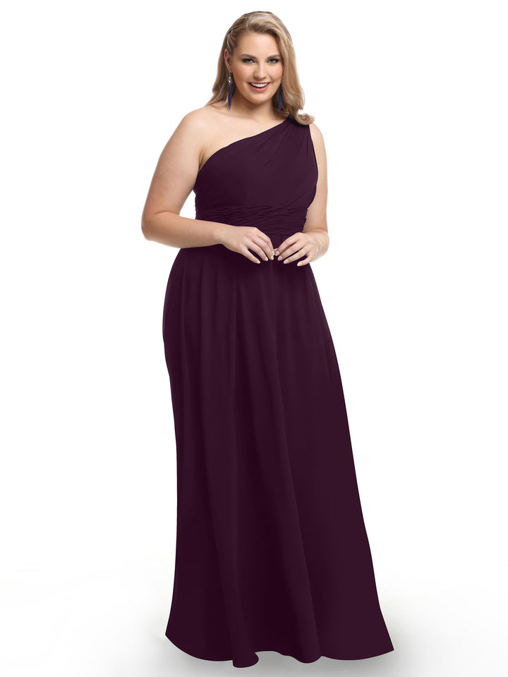 A woman in the Avery Austin 80047 floor-length aubergine one-shoulder chiffon dress with a ruched bodice stands smiling against a white background.