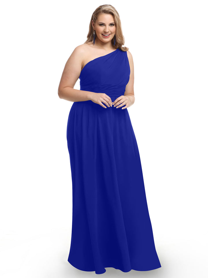 A woman wearing Avery Austin style 80047 in cobalt stands smiling against a plain white background, showcasing a modern twist on classic elegance with its one-shoulder chiffon design and ruched bodice.