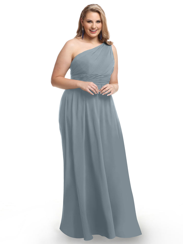 A woman in Avery Austin style 80047, a light blue one-shoulder chiffon dress with a ruched bodice, stands smiling against a plain white background.