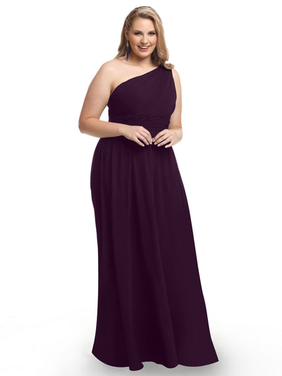 A woman wearing Avery Austin’s 80047—a long, dark purple one-shoulder chiffon dress with a modern cut-out—stands smiling against a plain white background.