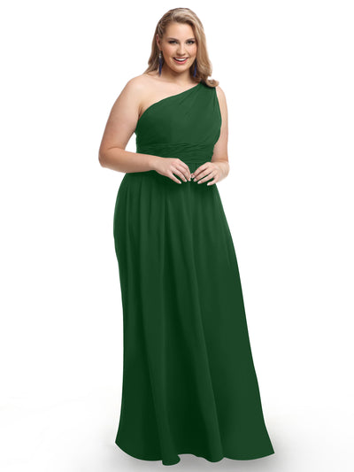A woman wearing Avery Austin style 80047—a dark green one-shoulder chiffon dress with a modern cut-out—stands smiling, hands together, in front of a plain white background.