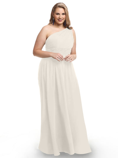 A woman smiles against a white background, wearing Avery Austin style 80047—a long, elegant one-shoulder chiffon dress with a modern twist. She has wavy light brown hair and holds her hands together in front of her.