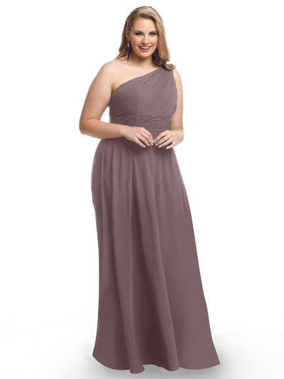 A woman with long, wavy blonde hair smiles in the Avery Austin 80047, a mauve one-shoulder floor-length chiffon dress, standing against a plain white background.