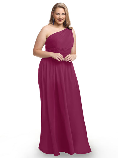 A woman stands smiling with her hands clasped in front of her, modeling Avery Austin’s 80047—a sleeveless, floor-length magenta one-shoulder chiffon dress with a modern twist and ruched bodice—against a plain white background.