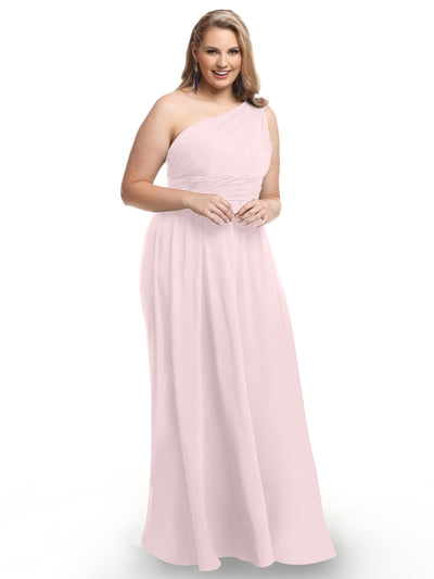 A woman models Avery Austin’s 80047, a light pink one-shoulder chiffon dress with a ruched bodice, standing and smiling against a plain white background.
