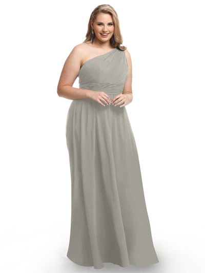 A woman smiles against a white background, wearing Avery Austin style 80047—a light gray, floor-length one-shoulder chiffon dress with a ruched bodice.