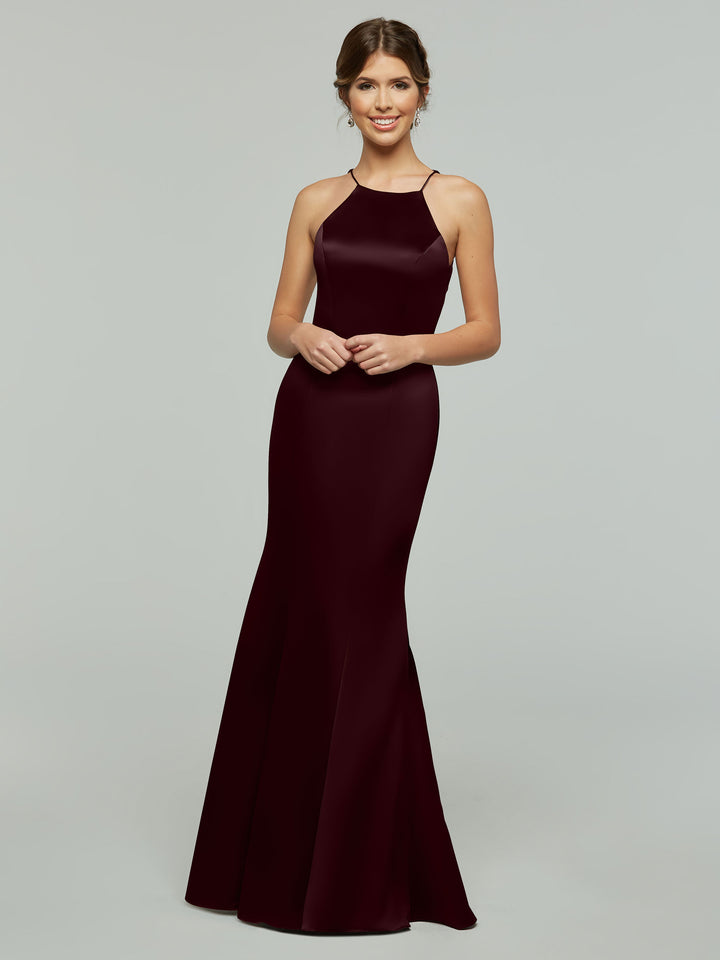 A woman stands smiling in Avery Austin’s 80071, a sleek floor-length burgundy gown with a fitted bodice, flared skirt, and halter neckline. Her hair is styled up with simple earrings against a plain light gray background.