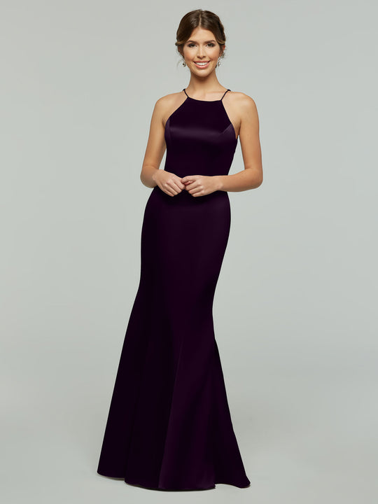 A woman smiles in the Avery Austin TH-80071, a sleek, floor-length eggplant gown with a fitted bodice and halter neckline, set against a plain light gray background.