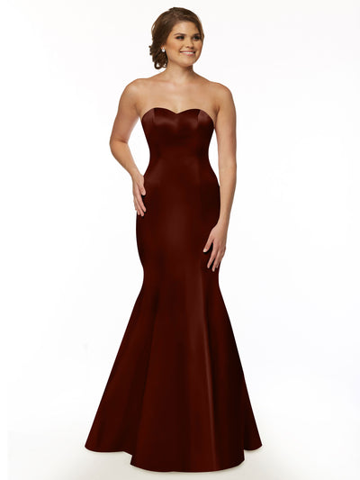 A woman in the Avery Austin 80072 burgundy gown, featuring a strapless sweetheart neckline, floor-length mermaid silhouette, and ruffled back, stands smiling with one hand on her hip against a plain white background.