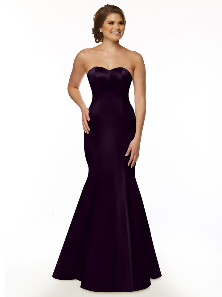 A woman wearing Avery Austin’s 80072 strapless sweetheart neckline, floor-length fit and flare dress in eggplant with a ruffled back smiles against a plain white background.