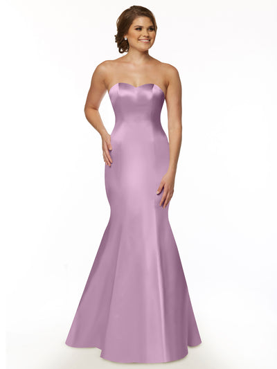 A woman poses against a white background, smiling with one hand on her hip, wearing Avery Austin's 80072—a lilac, strapless sweetheart neckline fit and flare floor-length dress.