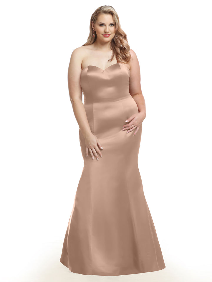 A woman poses against a plain white background in the Avery Austin 80072 strapless, fitted, floor-length satin bridesmaid dress in Buff.