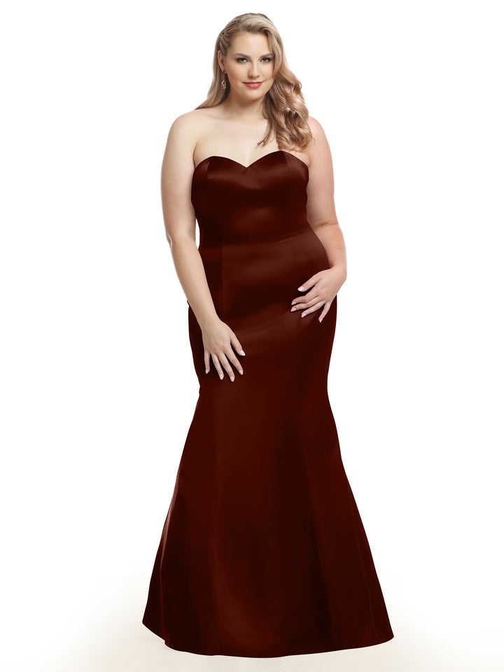 A woman with long, wavy blonde hair models the Avery Austin TH-80072 strapless satin mermaid bridesmaid dress in burgundy, standing elegantly against a plain white background.