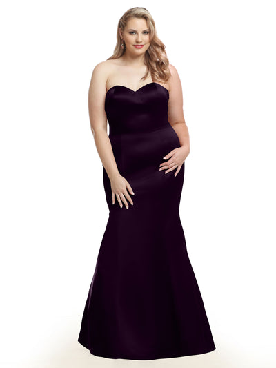 A woman models Avery Austin’s 80072, a black satin strapless mermaid bridesmaid dress with a subtle flare, standing gracefully against a plain white background with long, wavy blonde hair.