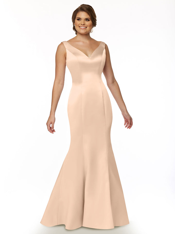 A woman in the Avery Austin 80078, a sleeveless blush fit and flare mermaid gown with a V-neck, stands smiling against a plain white background.