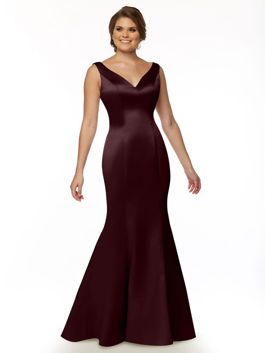A woman stands smiling against a white background, wearing the Avery Austin TH-80078, a sleeveless Bordeaux fit and flare mermaid gown with a V-neckline.