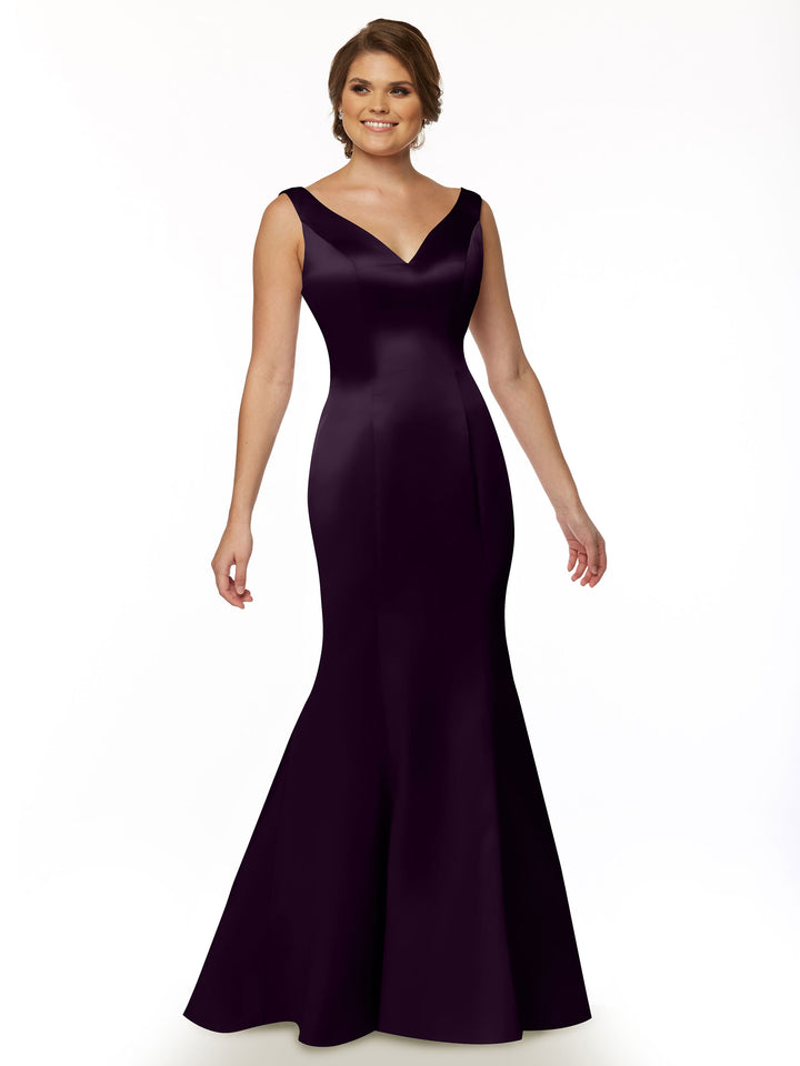 A smiling woman stands against a plain white background wearing Avery Austin style 80078, a sleeveless, floor-length deep purple fit and flare evening gown with a V-neckline and ruffled back.