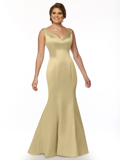 A woman models Avery Austin’s 80078—a sleeveless, light gold fit and flare mermaid gown with a V-neckline and ruffled back—posing against a white background, smiling with one arm relaxed and the other slightly bent.