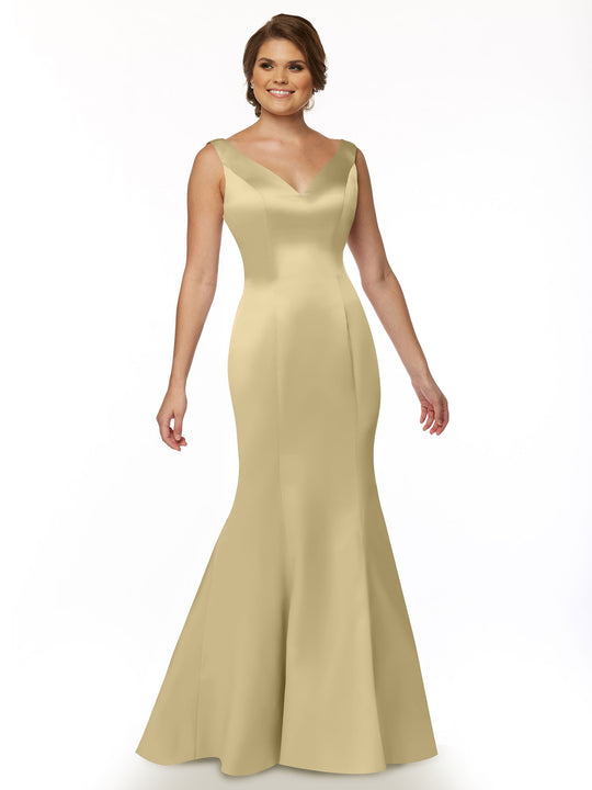 A woman models Avery Austin’s 80078—a sleeveless, light gold fit and flare mermaid gown with a V-neckline and ruffled back—posing against a white background, smiling with one arm relaxed and the other slightly bent.