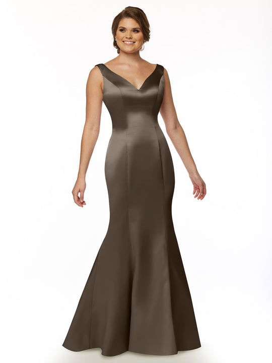 A woman smiles while standing against a white background, wearing Avery Austin’s 80078: a sleeveless, floor-length dark brown satin mermaid gown with a V-neckline and ruffled back.