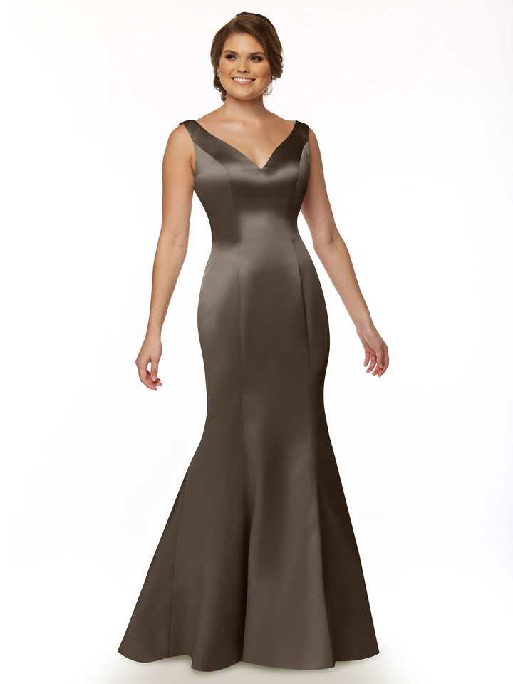 A woman smiles while standing against a white background, wearing Avery Austin’s 80078: a sleeveless, floor-length dark brown satin mermaid gown with a V-neckline and ruffled back.